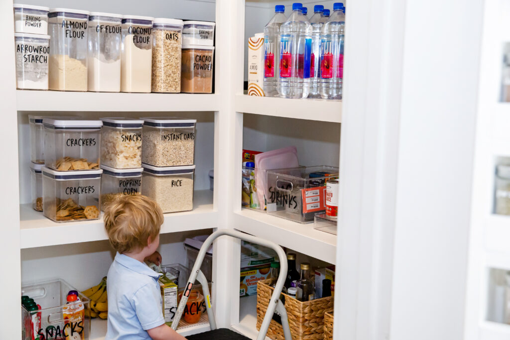 Child pulling a snack from a kid-height bin in a whole-family pantry, Houston home organizing by Wildely Organized